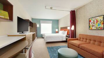 A hotel room with a bed, a desk, a television, a sofa, and a painting on the wall.