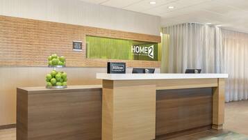 A hotel reception desk with a 'HOME2' sign, a 'Hilton Honors' badge, and a fruit display.