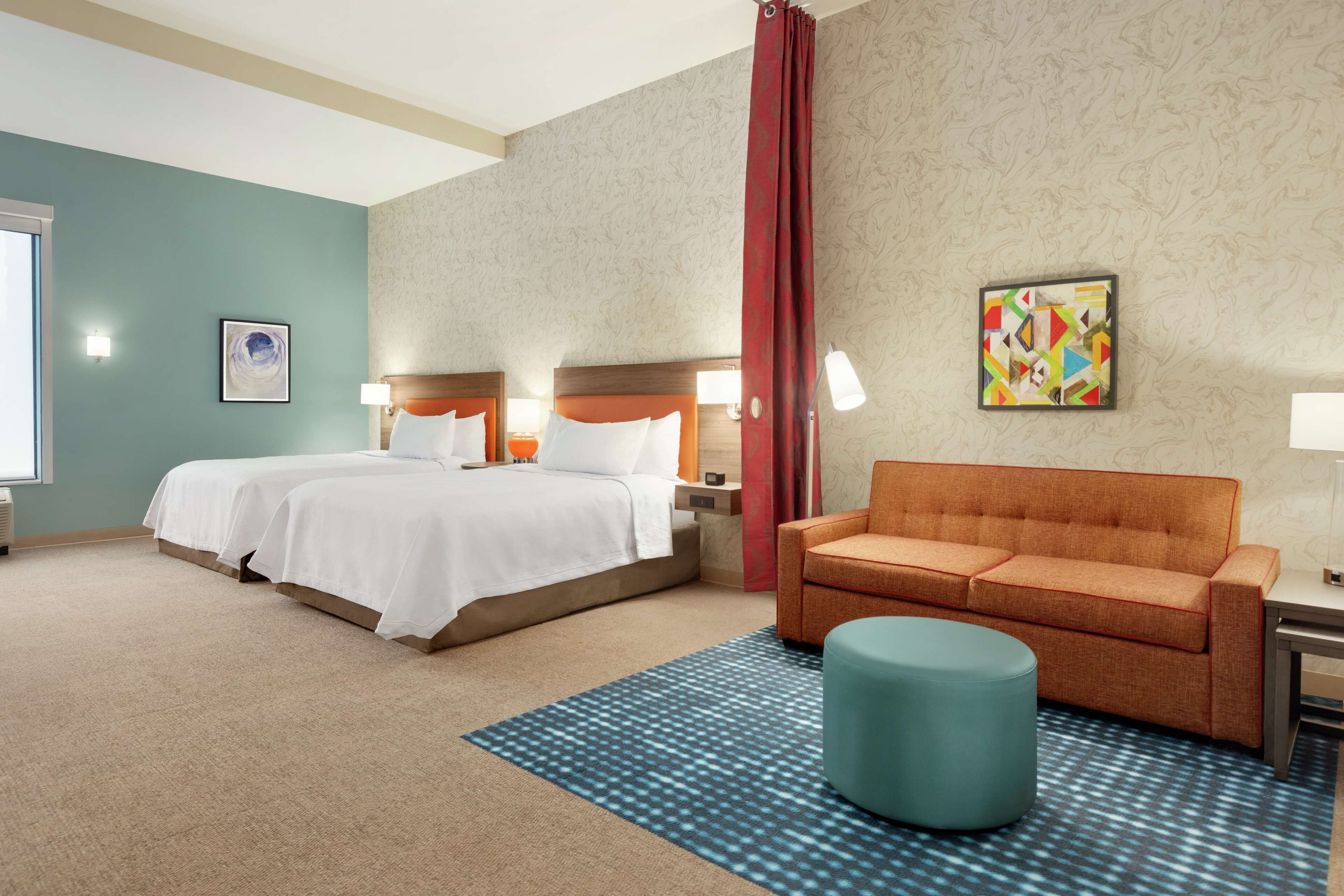 Een hotelkamer met twee bedden, een bank, een rond voetenbankje en een kamerkleed met een patroon.