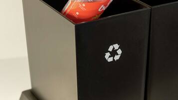 Una mano depositando una botella de plástico en un contenedor negro de reciclaje con el símbolo de reciclaje.