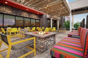 An outdoor seating area with yellow chairs, a fire pit, and a colorful striped sofa. - Home2 Suites by Hilton Greece Rochester (Rochester)
