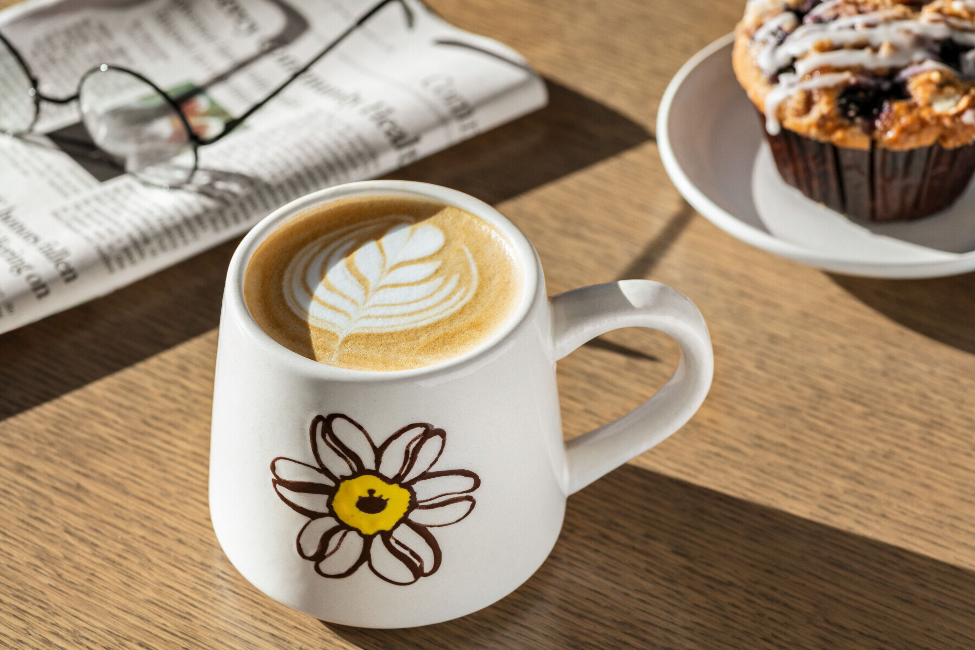 A white mug with a floral design and a coffee cup with latte art on a wooden table.