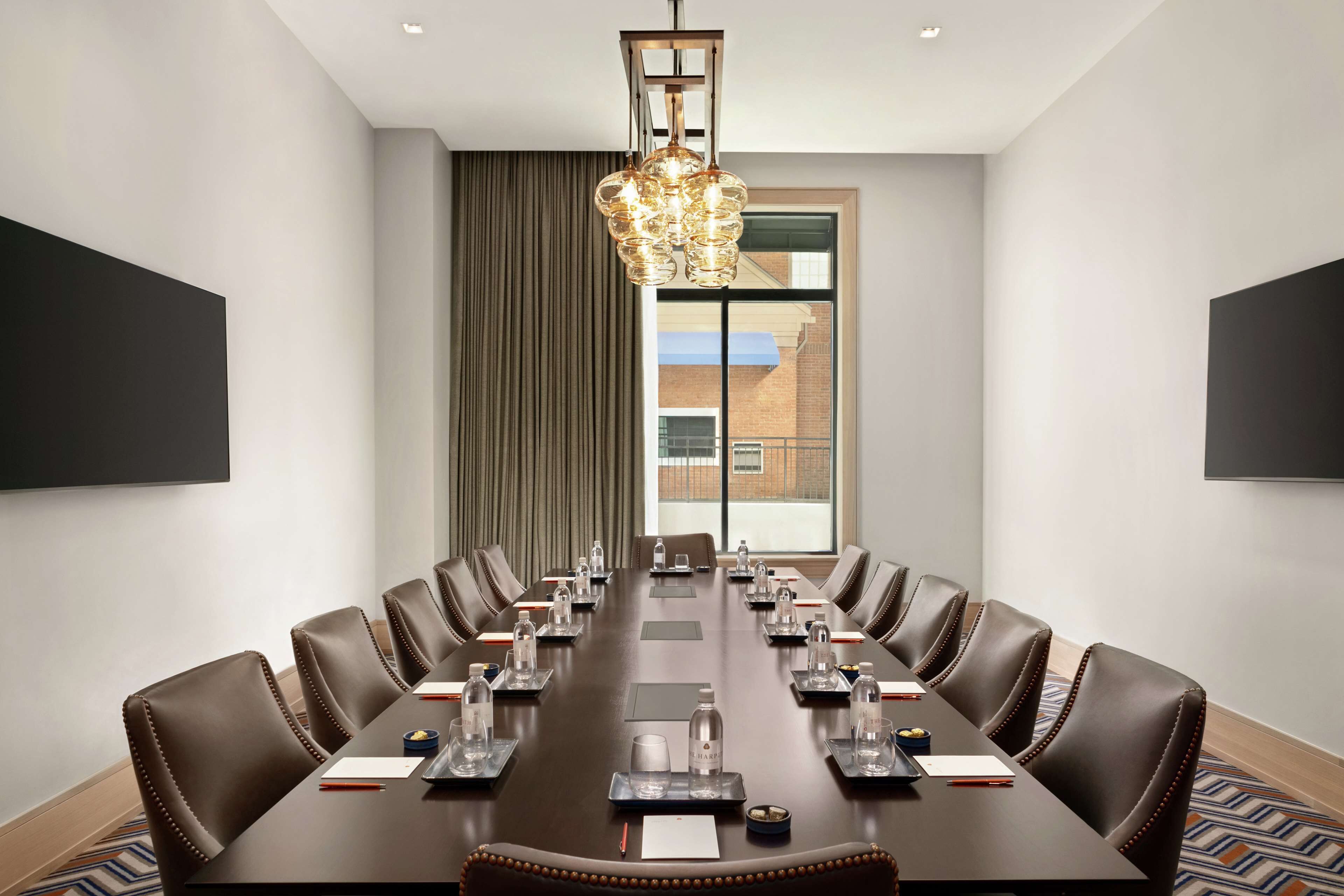 Une salle de conférence avec une longue table, des fauteuils en cuir, des bouteilles d’eau, des plaques nominatives et un lustre.