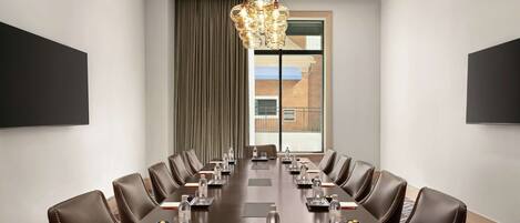 Une salle de conférence avec une longue table, des fauteuils en cuir, des bouteilles d’eau, des plaques nominatives et un lustre.
