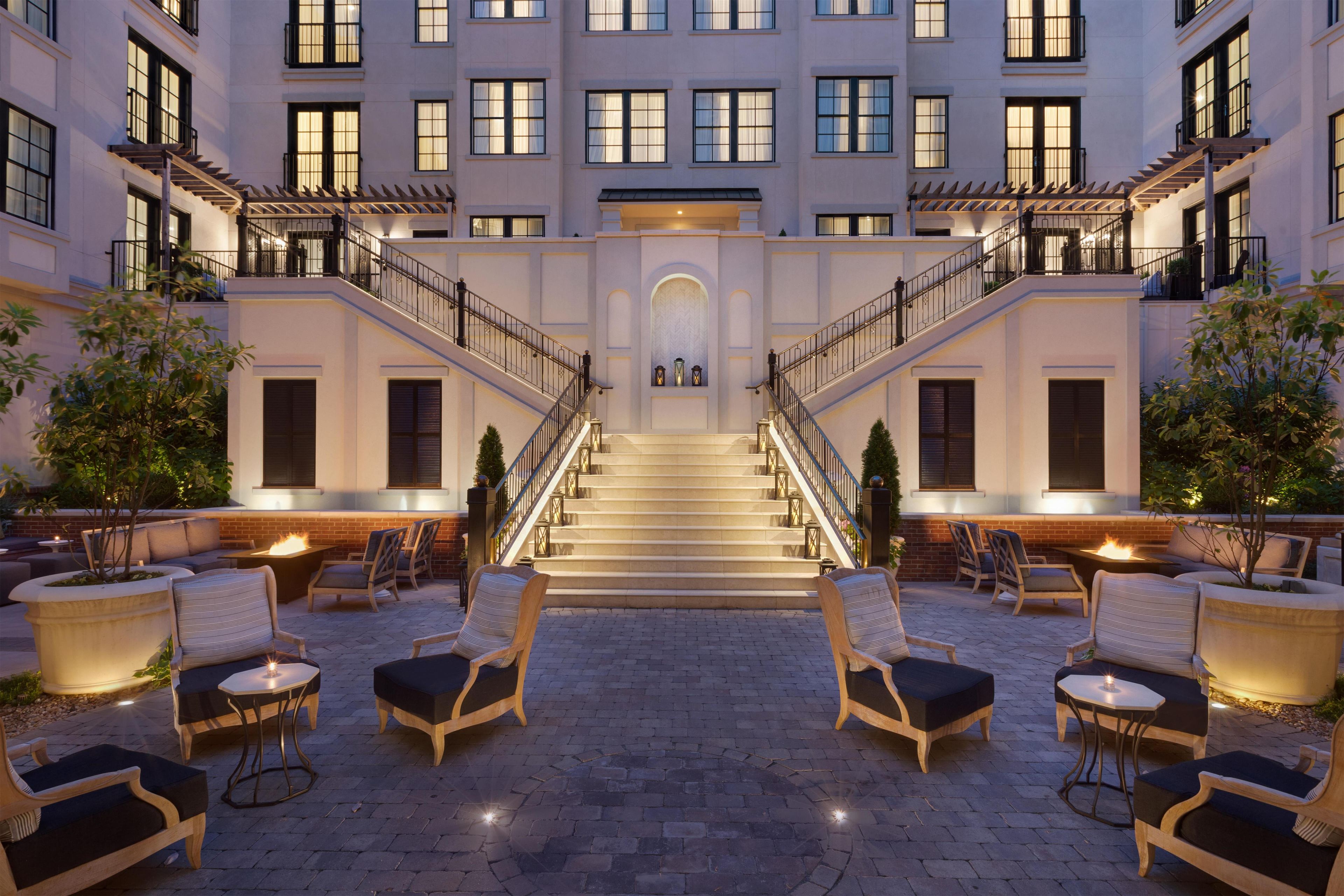 A hotel with a central staircase, outdoor seating area, and multiple windows.