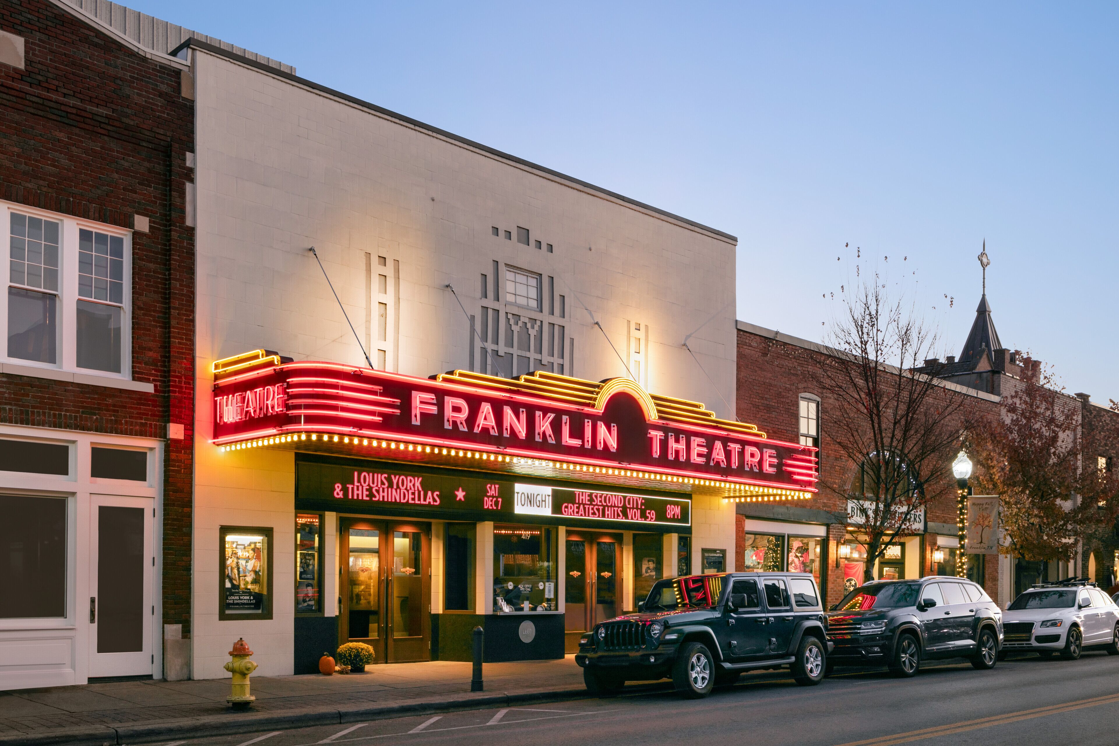 Un théâtre avec une enseigne lumineuse indiquant « FRANKLIN THEATRE » et un panneau annonçant « LOUIS YORK & THE SHINDELLAS ».