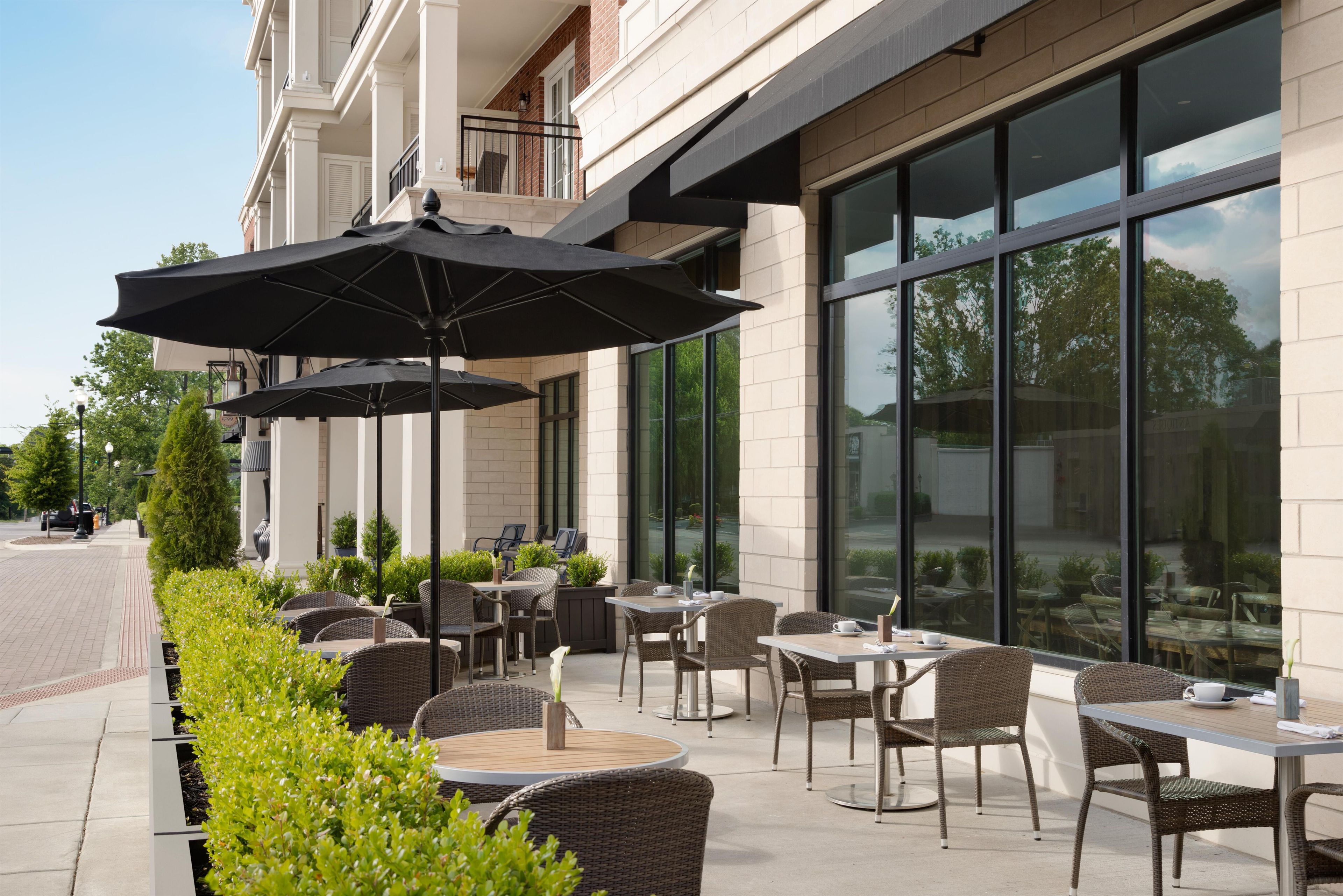 An outdoor seating area with tables and chairs, umbrellas, and a building facade with large windows.