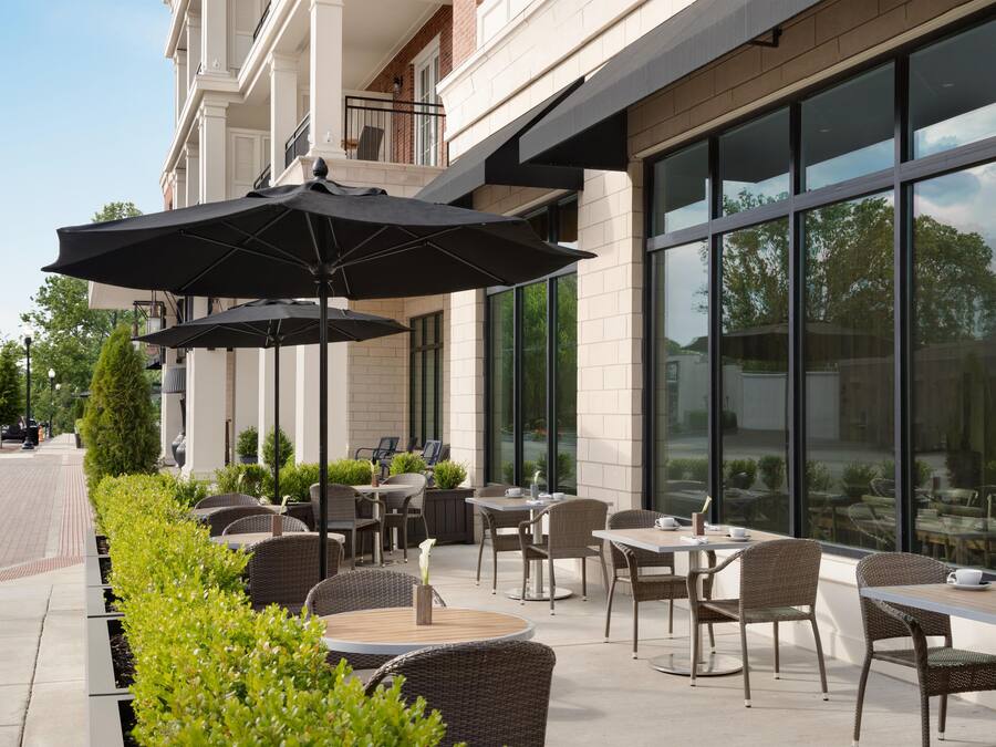 An outdoor seating area with tables and chairs, umbrellas, and a building facade with large windows.