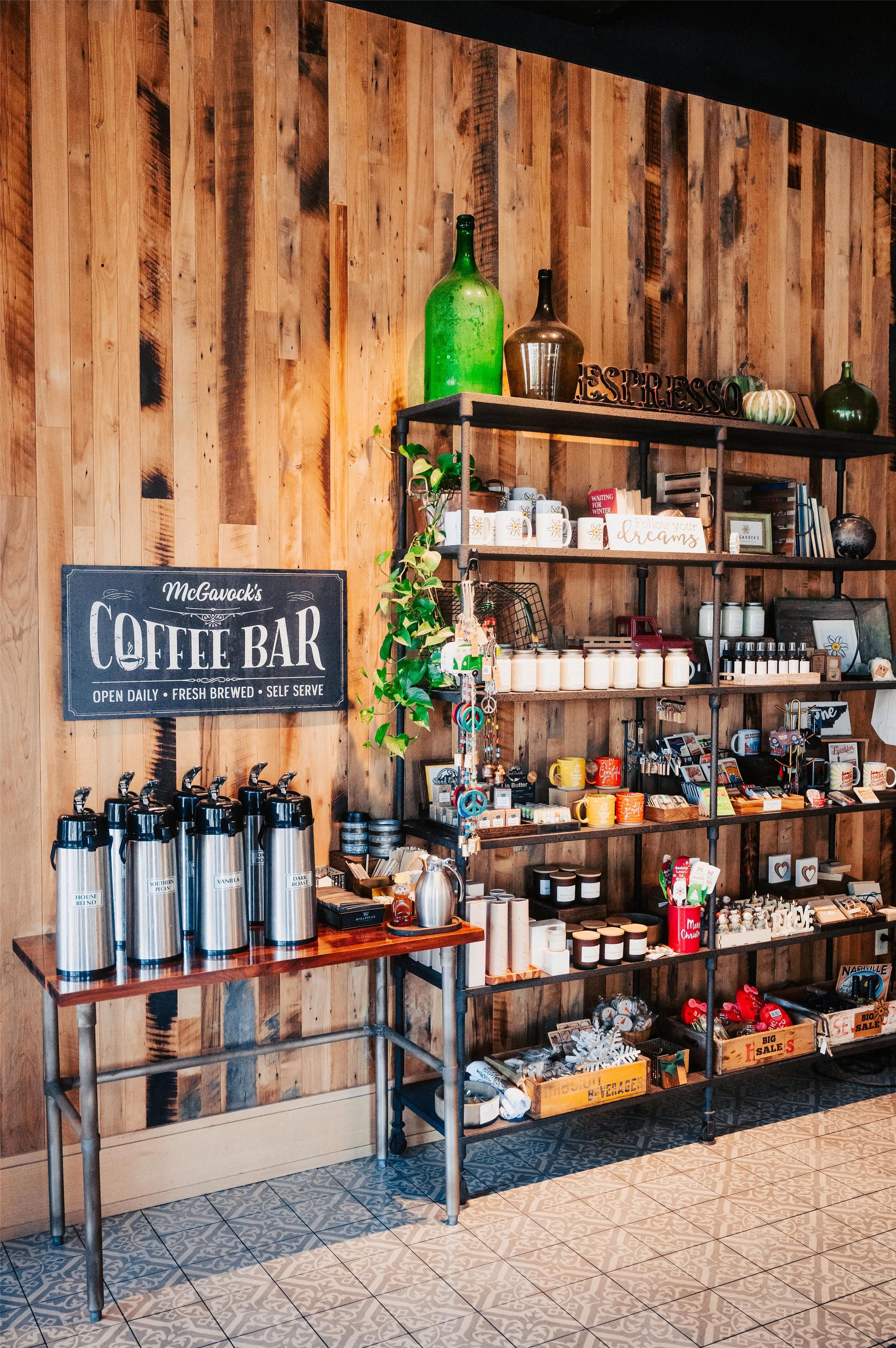 A coffee bar with a sign, shelves with mugs, and thermos bottles.