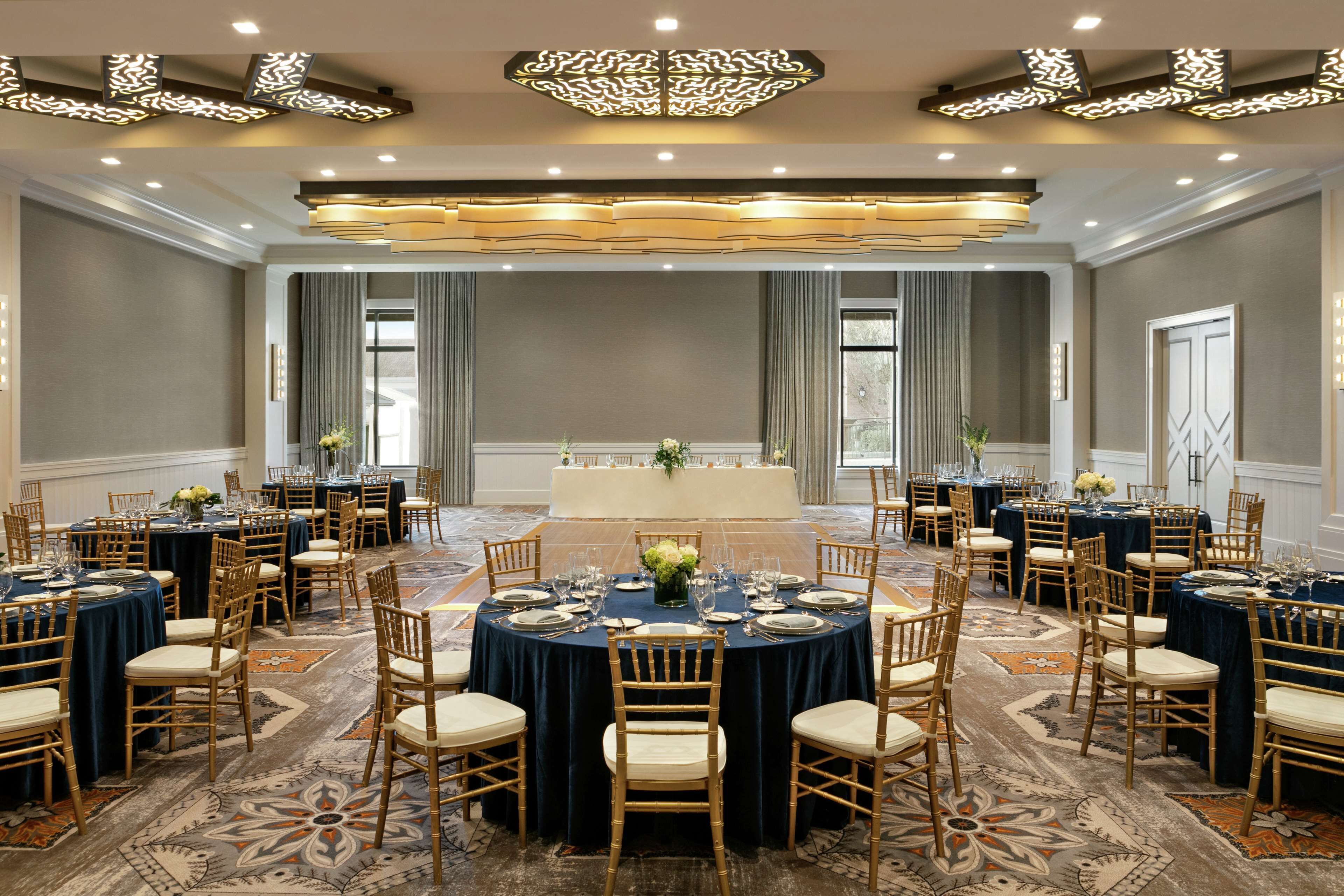 A large banquet hall with round tables, chairs, and a central stage.