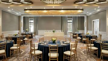 A large banquet hall with round tables, chairs, and a central stage.