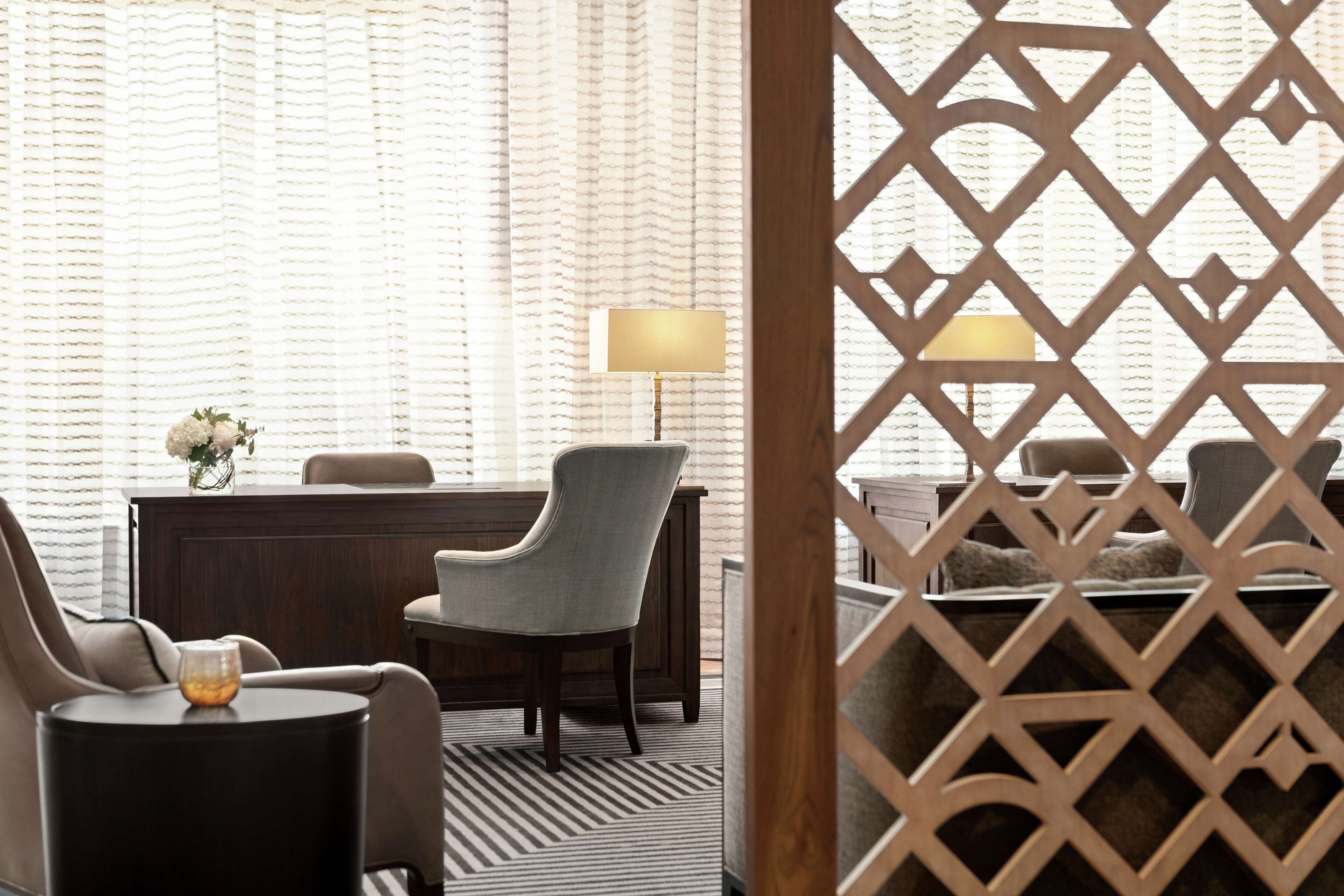 A hotel room with a desk, a chair, a lamp, and a decorative vase.