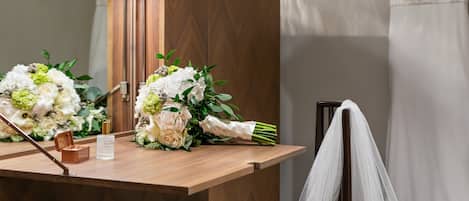 A wooden vanity with a mirror, a bouquet of flowers, and a bottle of perfume.