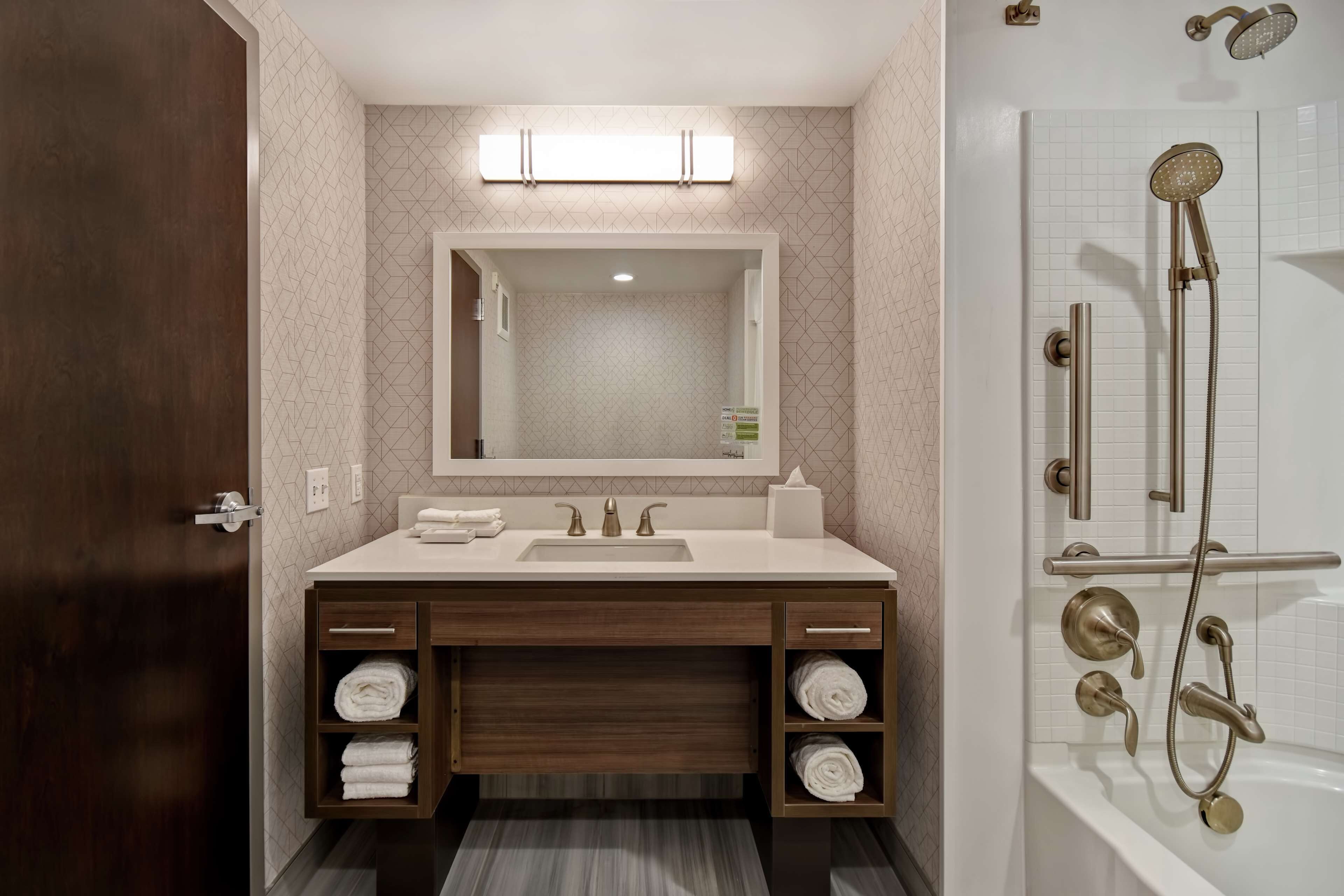 A modern bathroom with a wooden vanity, a large mirror, a white sink, and a separate shower area with a handheld showerhead.