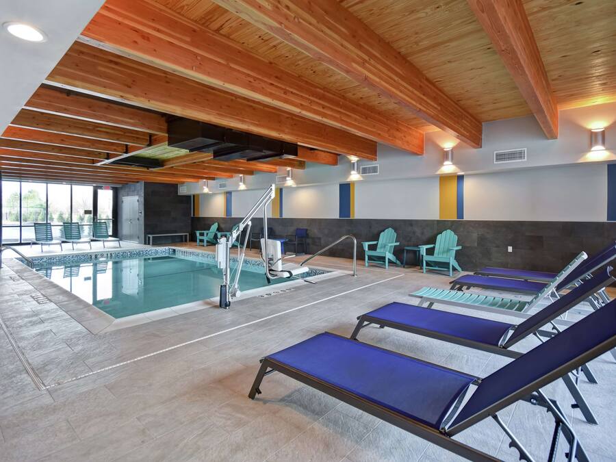 An indoor swimming pool with lounge chairs, wooden beams, and a tiled floor.