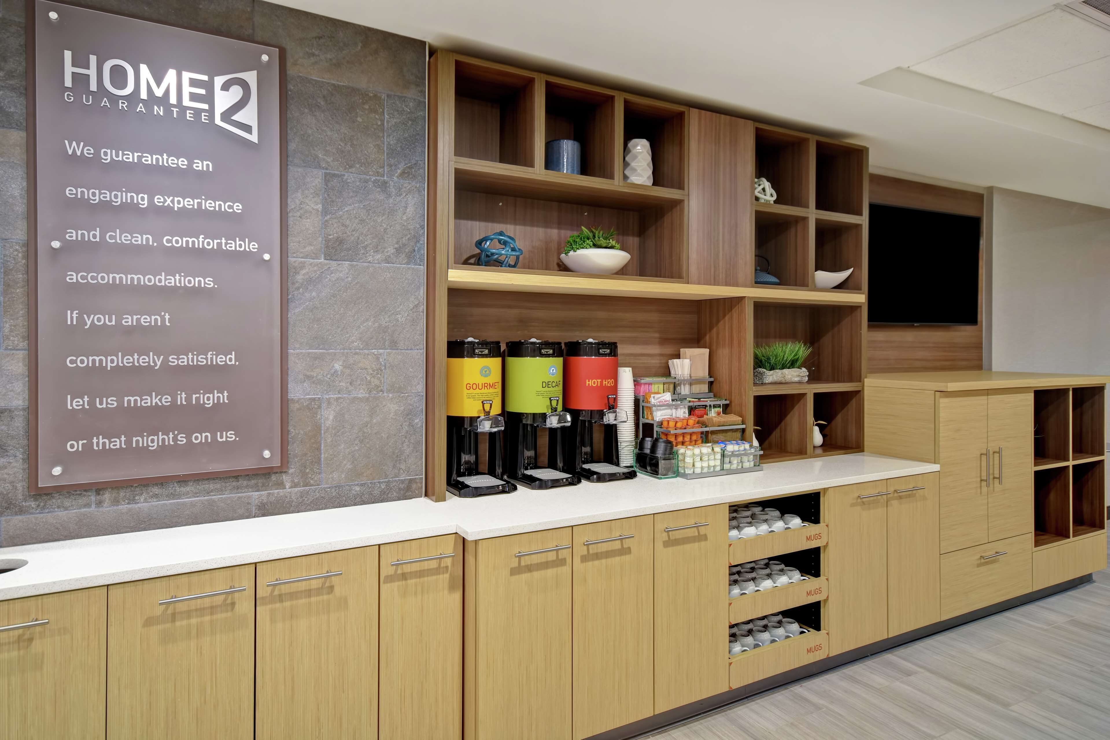 A modern kitchen area with a coffee station, storage cabinets, and a sign about the hotel's home guarantee.