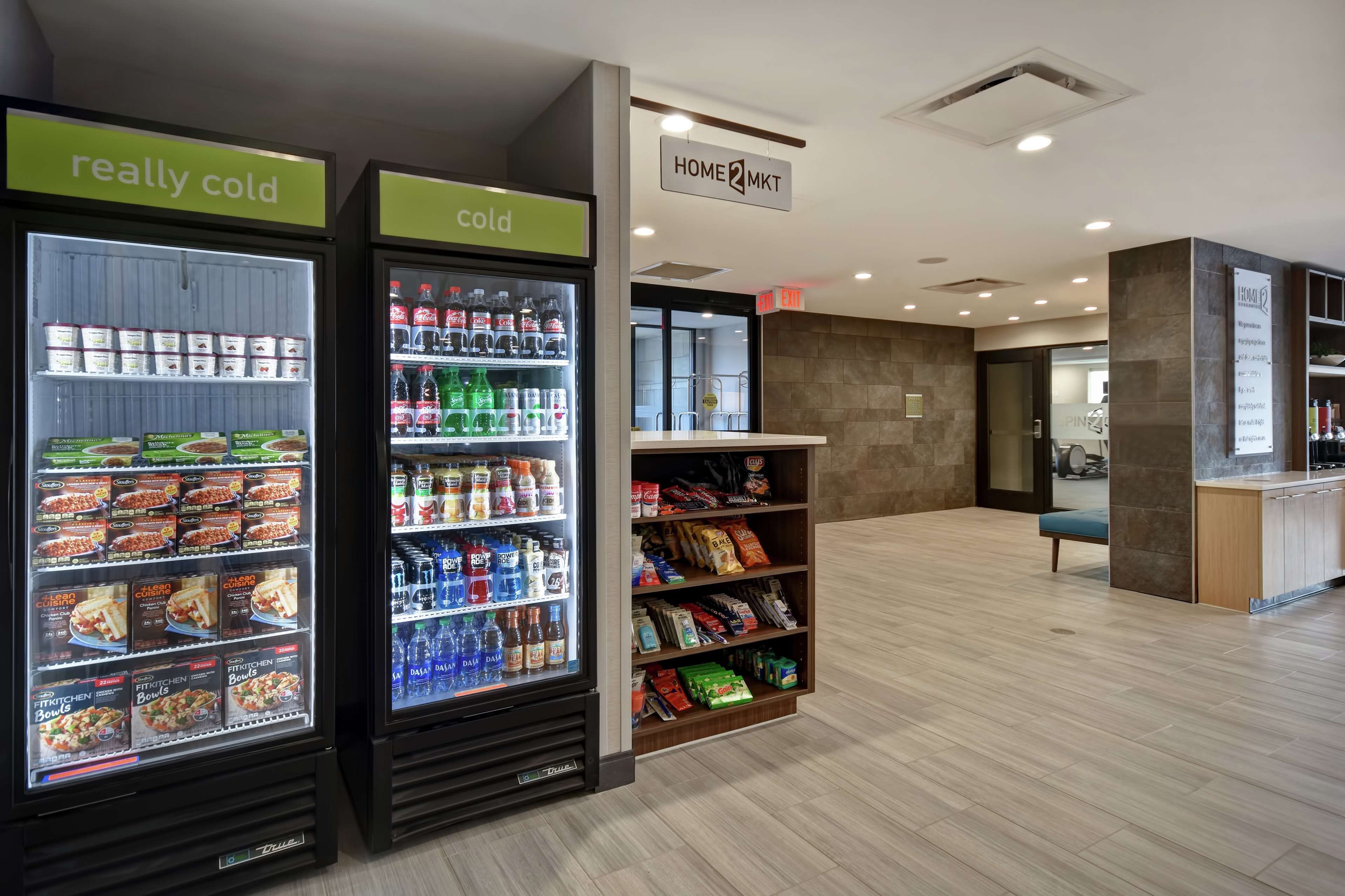 A modern hotel lobby with two refrigerated display cases labeled "really cold" and "cold," stocked with various food items and beverages.