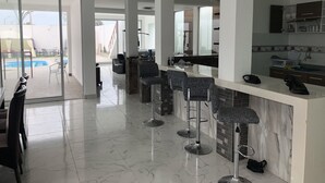 A modern kitchen with a marble countertop, a bar area with stools, and a view of a swimming pool. - New House by The Beach (Pisco)