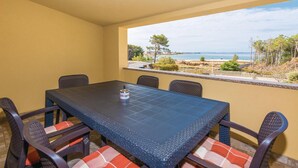Een eetgedeelte met een tafel en stoelen, uitzicht op zee, en een balkon met een hekwerk.