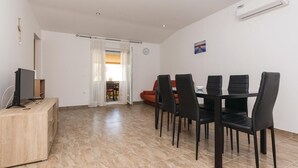Een eetgedeelte met een tafel en stoelen, een televisie op een houten kast, en een rode bank op de achtergrond.