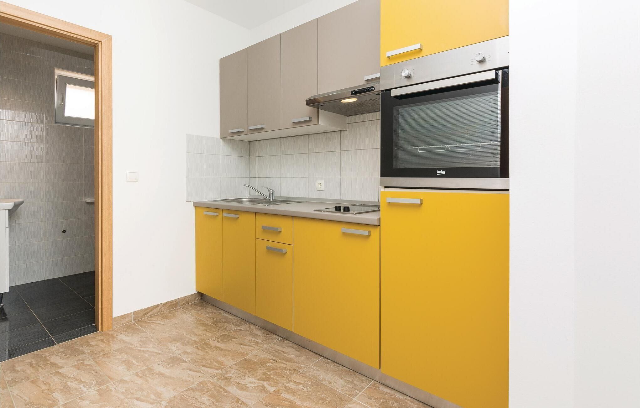 A kitchen with yellow cabinets, a stainless steel oven, and a window above the sink.