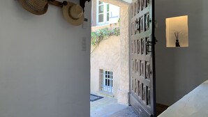 A hallway with a wooden shelf holding hats, a door with decorative panels, and a wall-mounted light fixture.