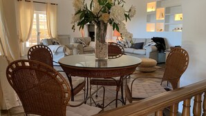 A dining area with wicker chairs, a glass table, and a vase of white flowers.