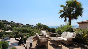 An outdoor seating area with wicker furniture, a stone table, and a view of the sea.