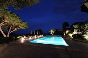 A nighttime swimming pool with lounge chairs and umbrellas, surrounded by trees and a view of the sea. - Villa sea view, quiet close to the center of Sainte Maxime. (Sainte-Maxime)