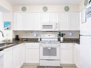 A kitchen with white cabinets, a microwave, an oven, and a granite countertop. - Ashworth 1006 (North Myrtle Beach)
