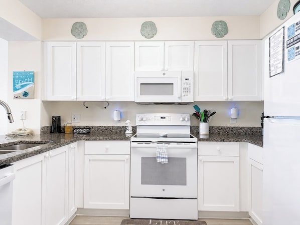A kitchen with white cabinets, a microwave, an oven, and a granite countertop.