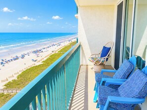 A balcony with a view of a beach, a chair, and a sofa.