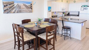 A dining area with a table and chairs, a kitchen with white cabinets, and a ceiling fan.
