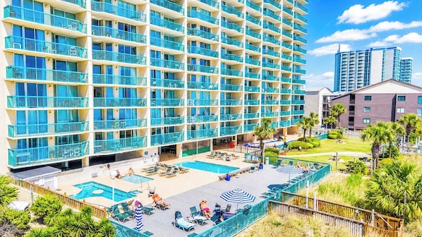 A multi-story hotel with balconies, a pool area, and a landscaped garden.