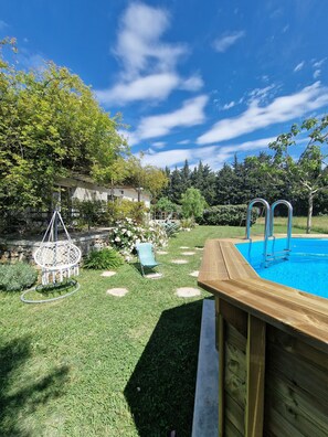 A backyard with a wooden deck, a swimming pool, a hanging chair, and a garden with various plants and trees. - Villa in the countryside with views of the Alpilles.  (Mouriès)