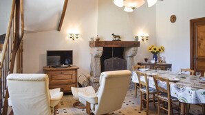 A cozy dining area with a stone fireplace, wooden furniture, and a television on a wooden cabinet. - Cozy home in Plancoet with WiFi (Plancoet)