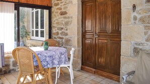 A stone-walled room with a wooden door, a table with a patterned tablecloth, wicker chairs, and a potted plant. - Cozy home in Plancoet with WiFi (Plancoet)