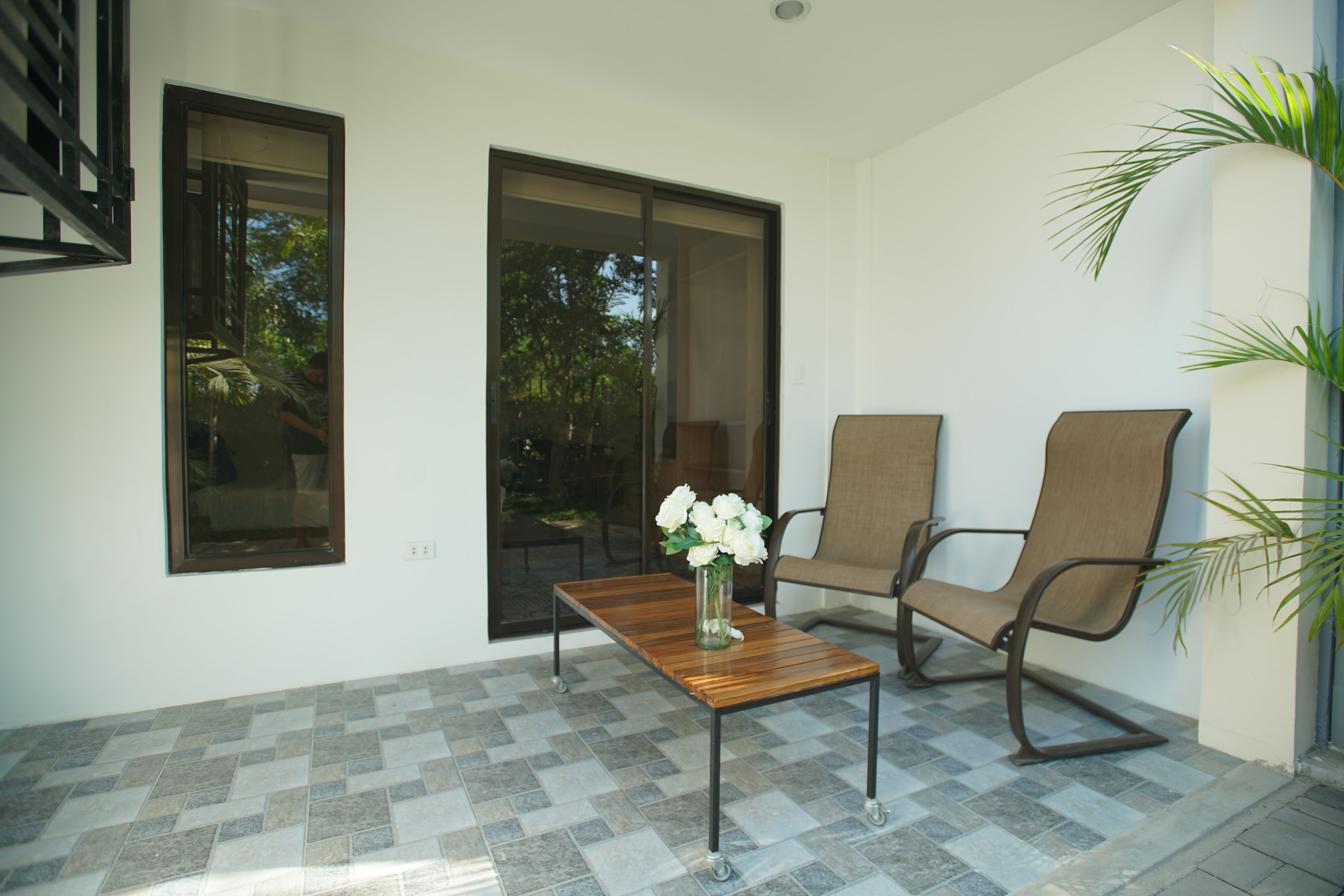 A patio with a wooden table, two chairs, and a vase of flowers.