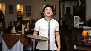 A person holding a tray in a restaurant with tables set for dining, a bar area, and various decorations on the walls. - Segara Residencias (Olongapo)