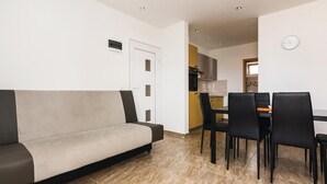 En moderne stue med sofa og spiseplads, med et køkken i baggrunden.