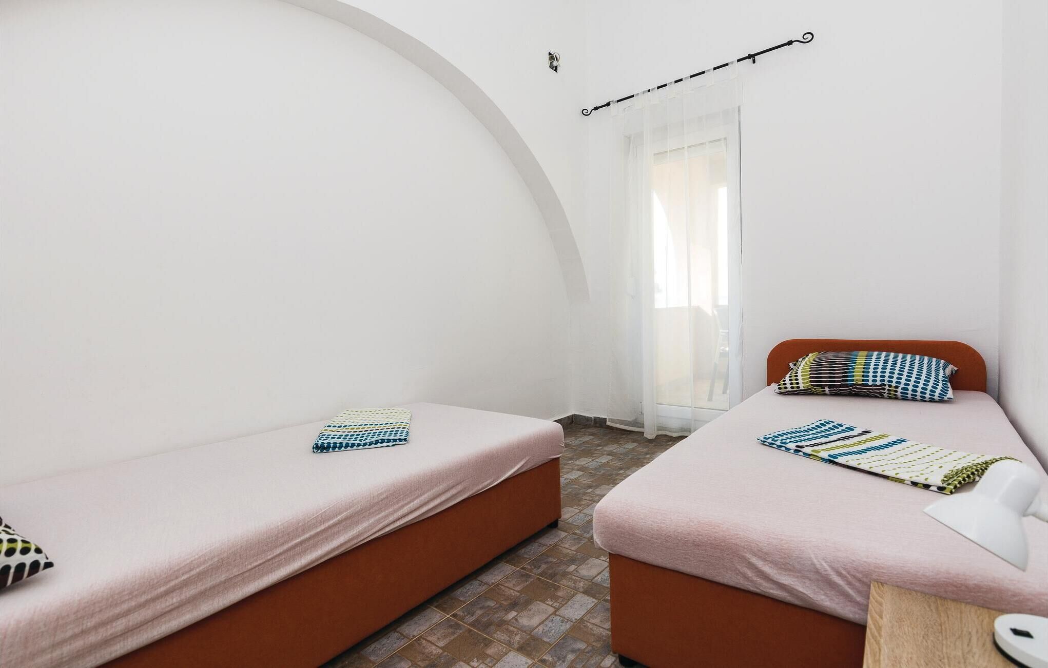 Quarto com duas camas, cada uma com colchão rosa e almofadas estampadas. As paredes são brancas e o teto é arredondado.
