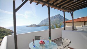Mesa de vidrio con sillas en un balcón con vistas a la costa y montañas.