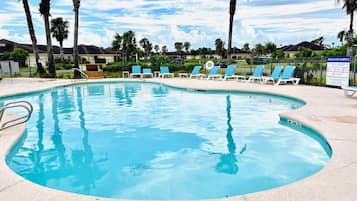 Relax by the clear pool surrounded by lounge chairs and a low wall.