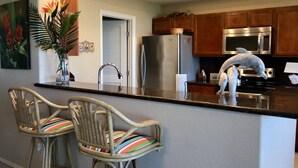 A kitchen with two wicker bar stools, a refrigerator, a microwave, and a decorative horse sculpture. - Half Moon Harbor- 15 HT (Laguna Vista)