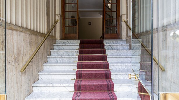 A marble staircase with red carpeted steps and brass handrails leading to a wooden door. - Casa Azzurra by Wonderful Italy (Genova)