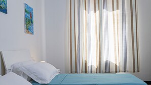 A bedroom with two beds, white pillows, a striped curtain, and a painting on the wall. - Casa Azzurra by Wonderful Italy (Genova)