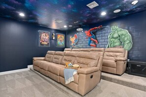 Un'area home theater con un divano reclinabile, un proiettore e un affresco raffigurante supereroi.