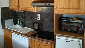 Una cocina compacta con armarios de madera, lavavajillas empotrado, estufa, cafetera y tostadora.