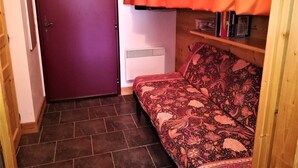 Una habitación pequeña y acogedora con una puerta morada, un sofá estampado y una cortina roja.