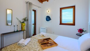 A bedroom with a bed, a bedside table, a mirror, a window with a view, and a ceiling with wooden beams.